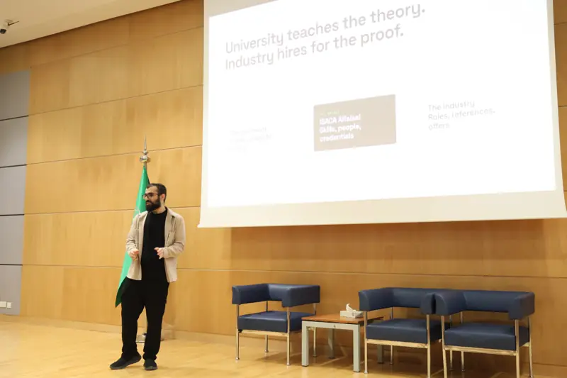A chapter organizer on stage beside a slide reading: University teaches the theory. Industry hires for the proof.